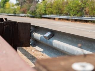 Close up of a guardrail with a 3M monitoring device for highway safety.