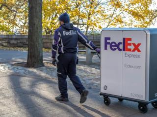 一个穿着联邦快递制服的人通过公园设置将带有FedEx Express徽标的高高推车拉动。