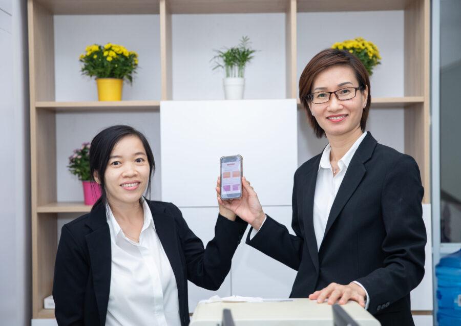 两个人拿着电话。它们后面的架子里有花朵。