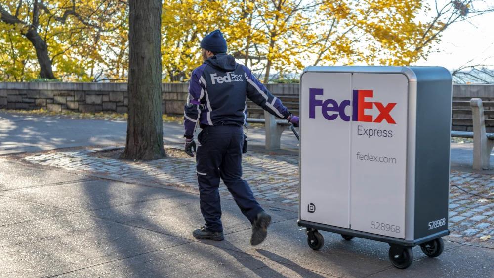 一个穿着联邦快递制服的人通过公园设置将带有FedEx Express徽标的高高推车拉动。