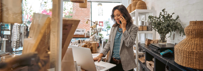 A person in a shop using a phone and working on a laptop